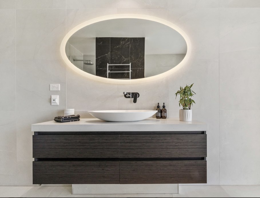 Dark timber floating vanity with backlit oval mirror